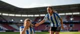 Fußballspielerin auf dem Platz hält Hand ans Auge nach einem Zusammenstoß, Teamkollegin eilt zu Hilfe