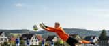 Amateurtorwart in orangem Trikot beim Hechtsprung in Stuttgarter Freizeitfußballspiel, grüner Rasen, Sonnenlicht