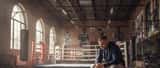 Male athlete sitting alone in a boxing gym reflecting, boxing gloves beside him, moody lighting