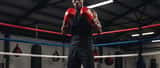 Young Black British boxer in training gloves standing in professional boxing ring in Manchester gym