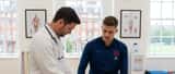 British male footballer on physio table being examined by sports medicine doctor in London clinic