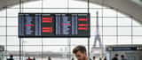 Voyageur inquiet à l'aéroport consultant son téléphone face à des vols annulés