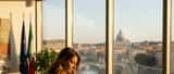 Avvocatessa italiana in un moderno studio legale a Roma con vista sul Tevere, revisione documenti, bandiera europea sullo sfondo