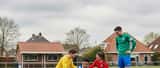 Groep amateurvoetballers op groen gras in Nederland, een speler houdt zijn enkel vast na een sliding tackle, teammates staan om hem heen