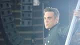 Robbie Williams optræder live ved udendørskoncert, syngende på scenen foran et stort publikum