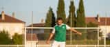 Joueur de football s'apprêtant à tirer un coup franc sur un terrain municipal en banlieue lyonnaise, lumière dorée du matin
