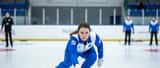 Curlingspelerska i leveransposition på is, inomhus idrottshall, fokuserat uttryck