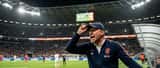 Nederlandse voetbaltrainer op de bank tijdens een wedstrijd, illustreert werkdruk en stress in topprestatie-omgevingen