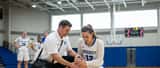 Female college basketball player holding her knee in pain as athletic trainer assesses the injury on court