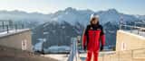 Österreichischer Wintersportler im Ski-Outfit am Abfahrtshang, österreichische Alpen im Hintergrund