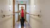Senior femme âgée marchant prudemment dans un couloir suisse, appui sur la paroi, style photo documentaire