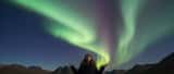 Person in glasses looking up at green and purple aurora borealis in a Scottish night sky