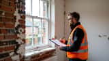 Building surveyor examining soot deposits on interior wall near window in a Northamptonshire terraced house after Corby industrial fire 2026