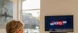 Nederlandse vrouw kijkt televisie met NPO afstandsbediening in Amsterdamse woning