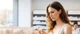 Mulher portuguesa examinando o rótulo de um produto cosmético numa farmácia com expressão preocupada
