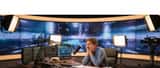 Journaliste de télévision fatigué assis à son bureau de studio en soirée