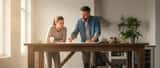 Handwerker bespricht Renovierungspläne mit Hausbesitzer am Tisch