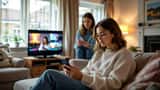 British teenager scrolling social media app on smartphone with concerned parent looking on in living room