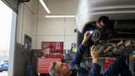 Australian mechanic inspecting a car on a hoist in a suburban Sydney workshop, lying under the vehicle with a torch checking brake components