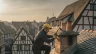 Ramoneur certifié sur le toit dune maison alsacienne à Strasbourg avec équipement de protection et brosse de ramonage