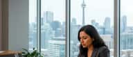 South Asian Canadian woman reviewing financial documents at a Toronto office desk with winter cityscape through windows