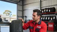 Australian tyre technician in red uniform inspecting a flat tyre removed from the rim in a suburban Melbourne tyre shop, professional diagnostic atmosphere