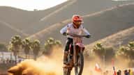 Piloto latino de motocross saltando en un circuito de tierra en California con polvareda y sol de tarde