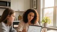 High school student and economics tutor reviewing supply and demand graphs at kitchen table in suburban Chicago