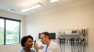 ENT otolaryngologist using an otoscope to examine a patient's ear in a modern US clinical setting