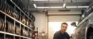 Gommista italiano al lavoro in un'officina pneumatici nella periferia di Milano, controllandendo un'auto sul ponte sollevatore
