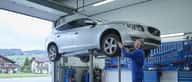 Mécanicien en coveralls bleus inspectant le dessous d'une voiture sur un pont élévateur dans un garage suisse à Lausanne