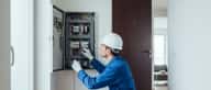 Elektriker in blauer Arbeitskleidung prüft einen Sicherungskasten in einer österreichischen Wohnung