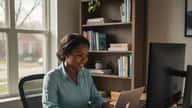 Black American woman working remotely on a laptop at a home office desk in Chicago with dual monitors and natural light