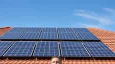 Australian homeowner looking up at newly installed solar panels on a terracotta-tiled suburban roof in bright midday sun