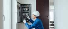Elektriker in blauer Arbeitskleidung prüft einen Sicherungskasten in einer österreichischen Wohnung