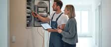 Elektriker erklärt einer Hauseigentümerin die Kosten am offenen Sicherungskasten in einer deutschen Wohnung