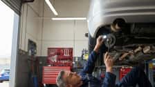 Australian mechanic inspecting a car on a hoist in a suburban Sydney workshop, lying under the vehicle with a torch checking brake components