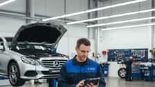 Australian mechanic using diagnostic tablet next to a Mercedes-Benz E-Class on a hydraulic lift in a Sydney automotive workshop