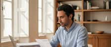 Homem português a analisar documentos fiscais numa secretária com computador portátil num escritório em Lisboa