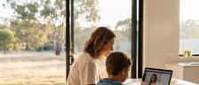 Australian mother and son sitting at a kitchen table looking at a laptop during an online tutoring session