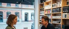 Kvinne leverer en smarttelefon med sprukket skjerm til en tekniker i et mobilverksted i Oslo