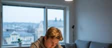 Norsk tenåring gjør lekser ved kjøkkenbordet i skandinavisk leilighet med varmt lampelys