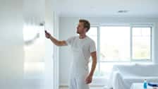 Professional Australian painter in white overalls applying fresh paint to a living room wall in a bright Melbourne home