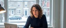 Femme québécoise révisant des documents financiers à sa table de cuisine à Montréal, ambiance concentrée et déterminée