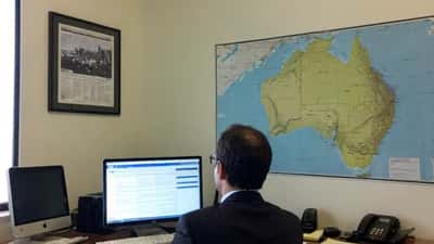 Australian solicitor reviewing international sanctions documents in a Sydney law office with Middle East news headlines on screen