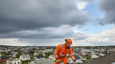 Norsk håndverker i orange verneutstyr inspiserer takskader på et hus i Stavanger etter storm