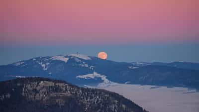 A large amber full moon rising at sunset behind the Swiss Alps, Chasseral