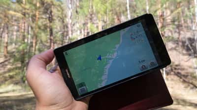 Älypuhelin GPS-navigaatiosovelluksella kädessä, taustalla järvimaisema