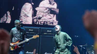 Oasis em show ao vivo no estádio, Liam Gallagher ao microfone cantando Wonderwall para uma multidão