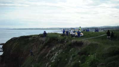HM Coastguard officers helping rescue a dog from a rocky cliff face